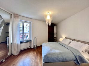 Un dormitorio con cama, ventana con cortinas, radiador, calefactor y escalera.
