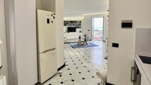 Une cuisine moderne avec un réfrigérateur blanc, un sol carrelé et une vue sur un espace de vie comprenant un canapé et une table à manger.