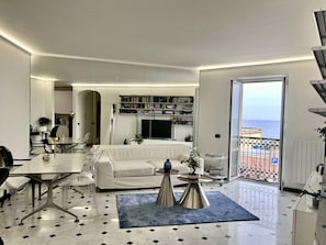 A modern hotel room with a balcony, a dining area, and a living space with a sofa and coffee table.