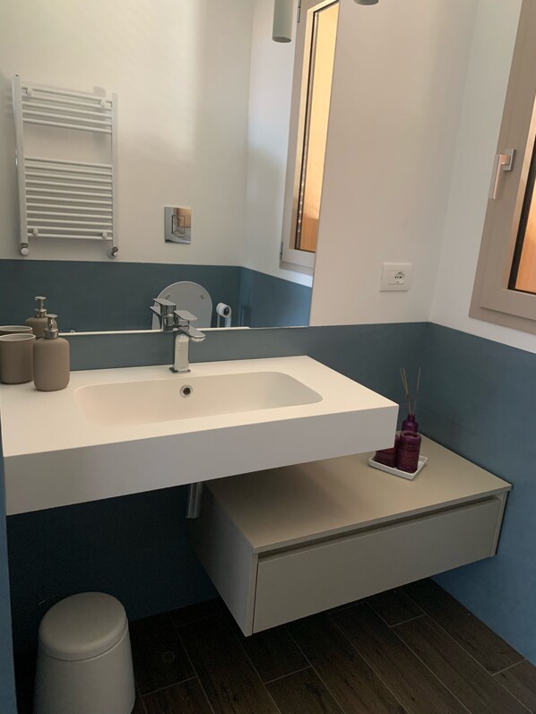 Une salle de bain moderne avec un lavabo blanc, un miroir, un porte-serviettes et une petite poubelle.