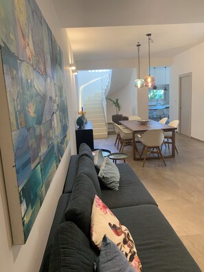 Ein modernes Wohnzimmer mit einem dunkelgrauen Sofa, einem Essbereich mit Holztisch und Stühlen sowie einer Treppe zu einer oberen Ebene.