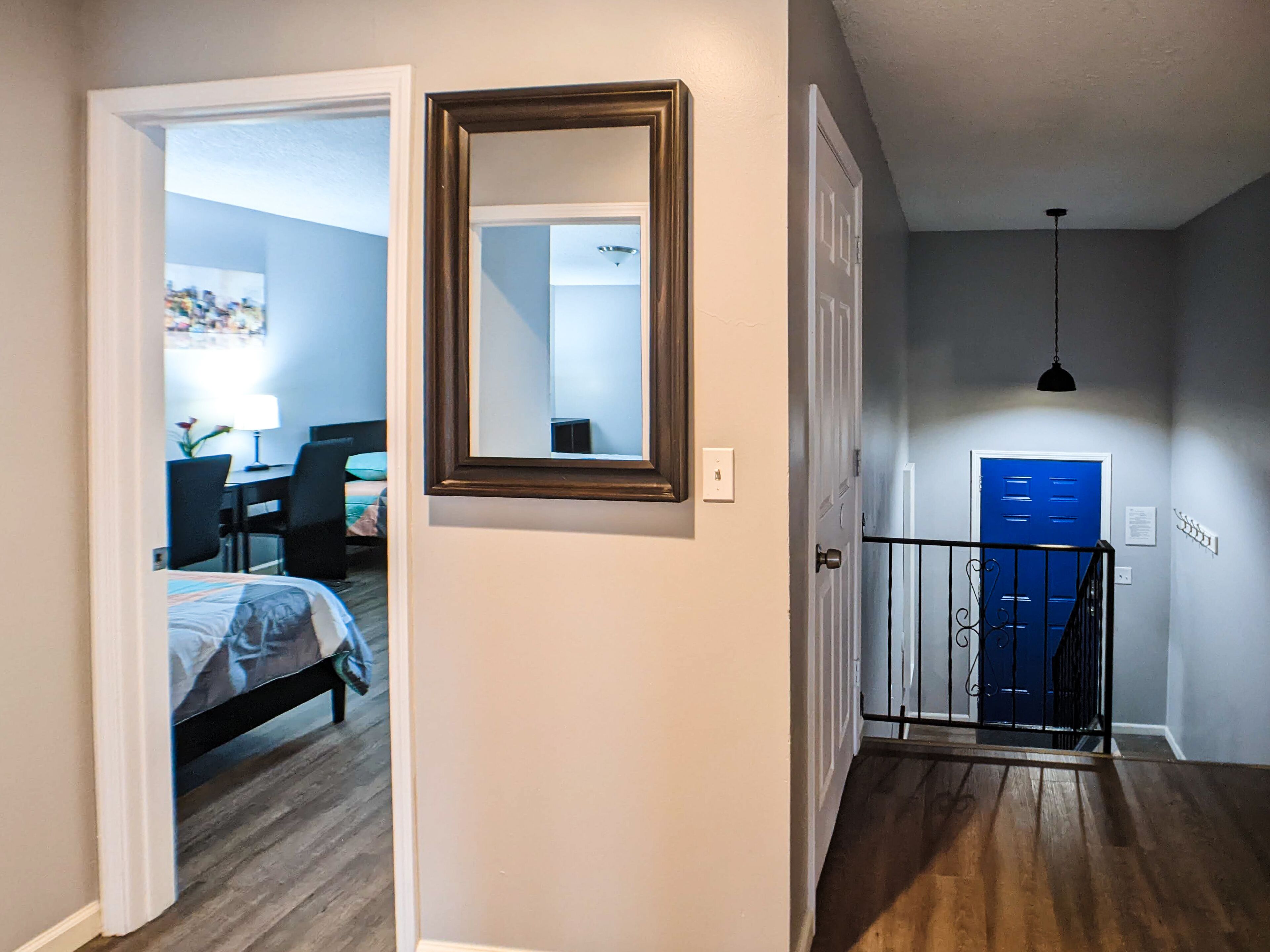 Un couloir avec une porte donnant sur une chambre, une porte bleue, une petite table et un luminaire suspendu.