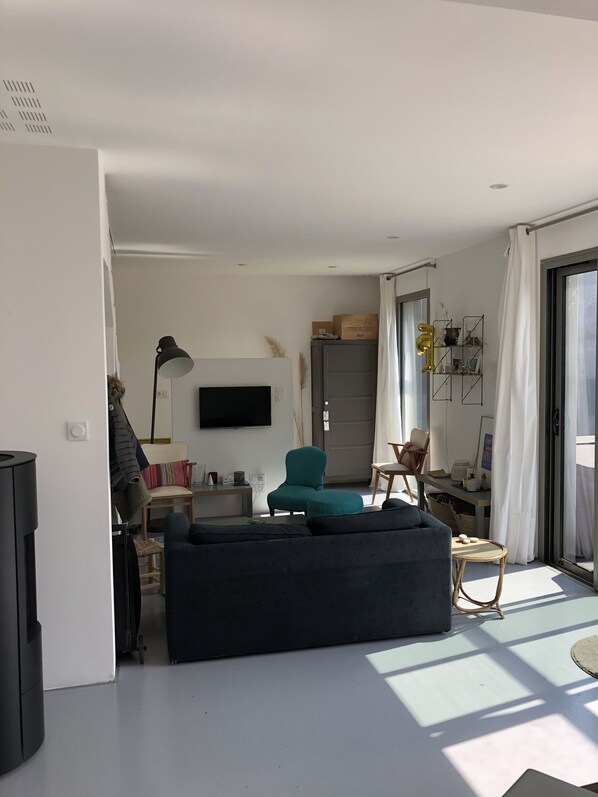 A modern living room with a sofa, a teal armchair, a flat-screen TV, and a dining area with a table and chairs.