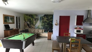 A living room with a pool table, a sofa, a dining table with chairs, a kitchen area with a microwave, and a red door. - Beautiful, quiet house for 4 to 6 people. 15mn Vallée des Singes - 25mn Futuroscope (Vivonne)