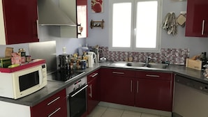A compact kitchen with red cabinets, a microwave, an oven, a sink, and a window with a view of the outside. - Beautiful, quiet house for 4 to 6 people. 15mn Vallée des Singes - 25mn Futuroscope (Vivonne)