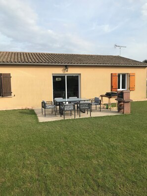 A building with a tiled roof, a sliding glass door, and a patio area with a table and chairs.