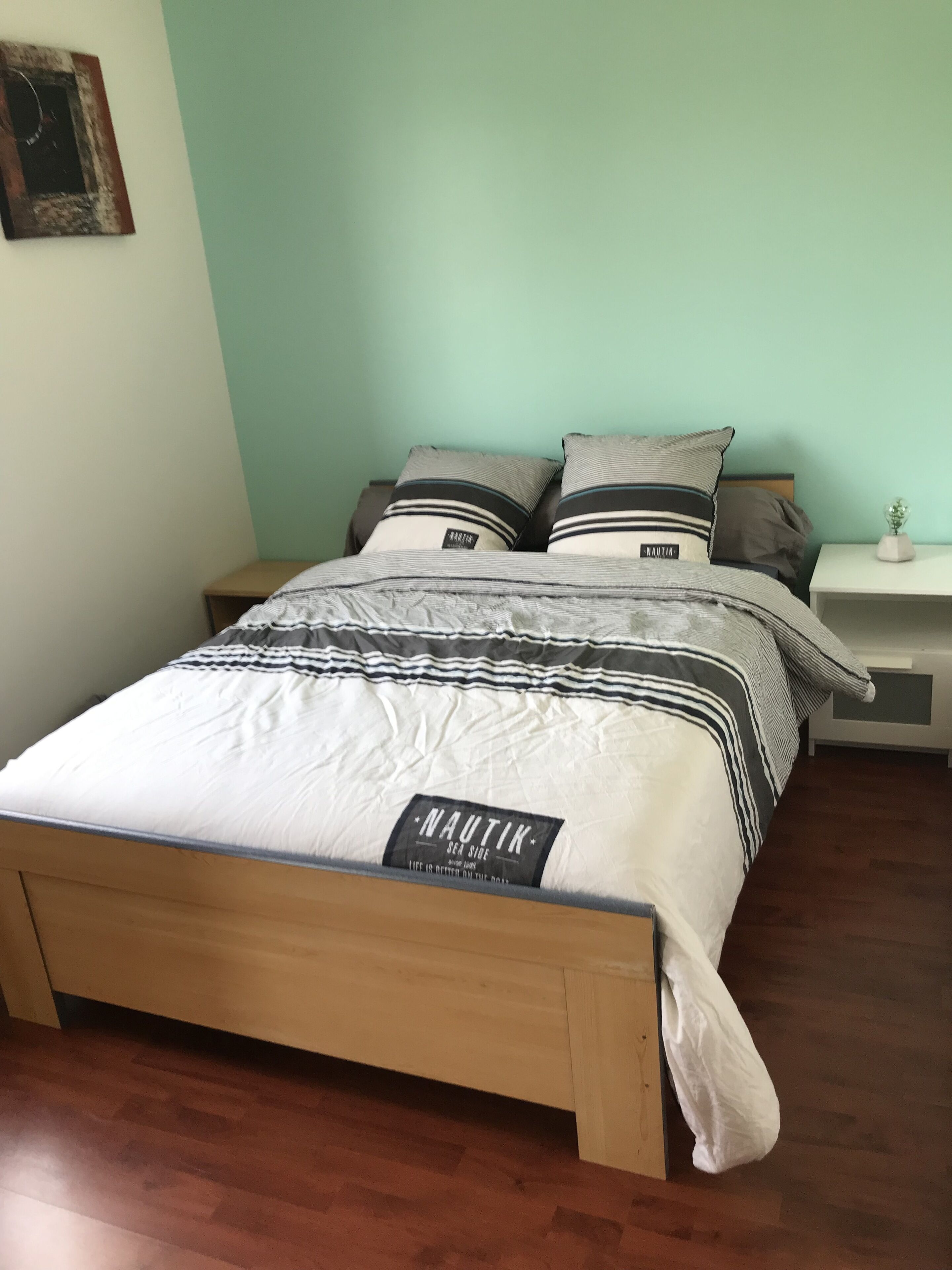 A bed with a Nautik branded mattress, a wooden headboard, and a nightstand with a small plant.