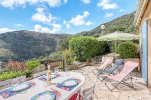 An outdoor dining area with a table set for two, surrounded by lounge chairs and a stone patio.