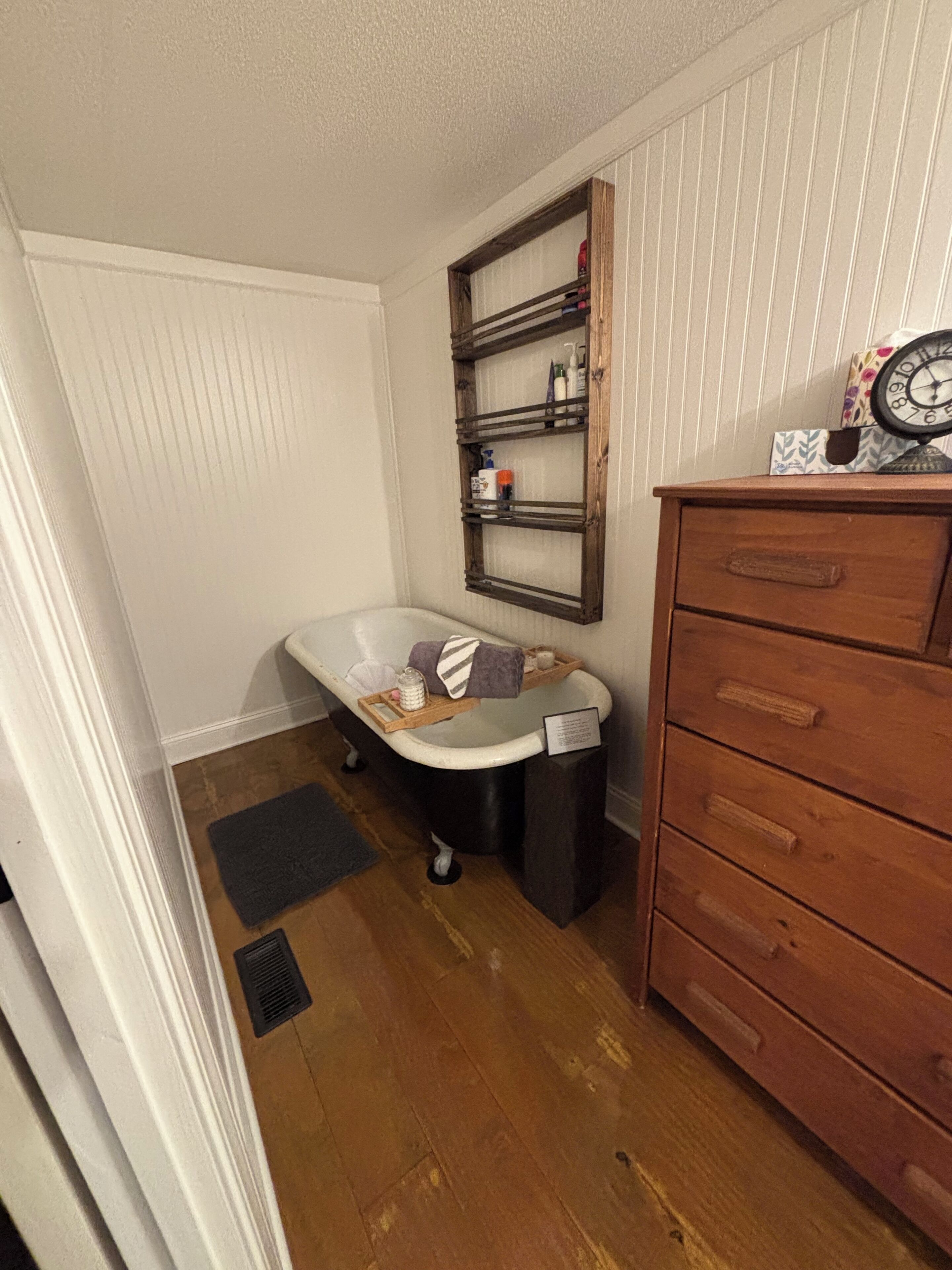 A bathroom with a bathtub, wooden shelves, a wooden dresser, and a clock on top.
