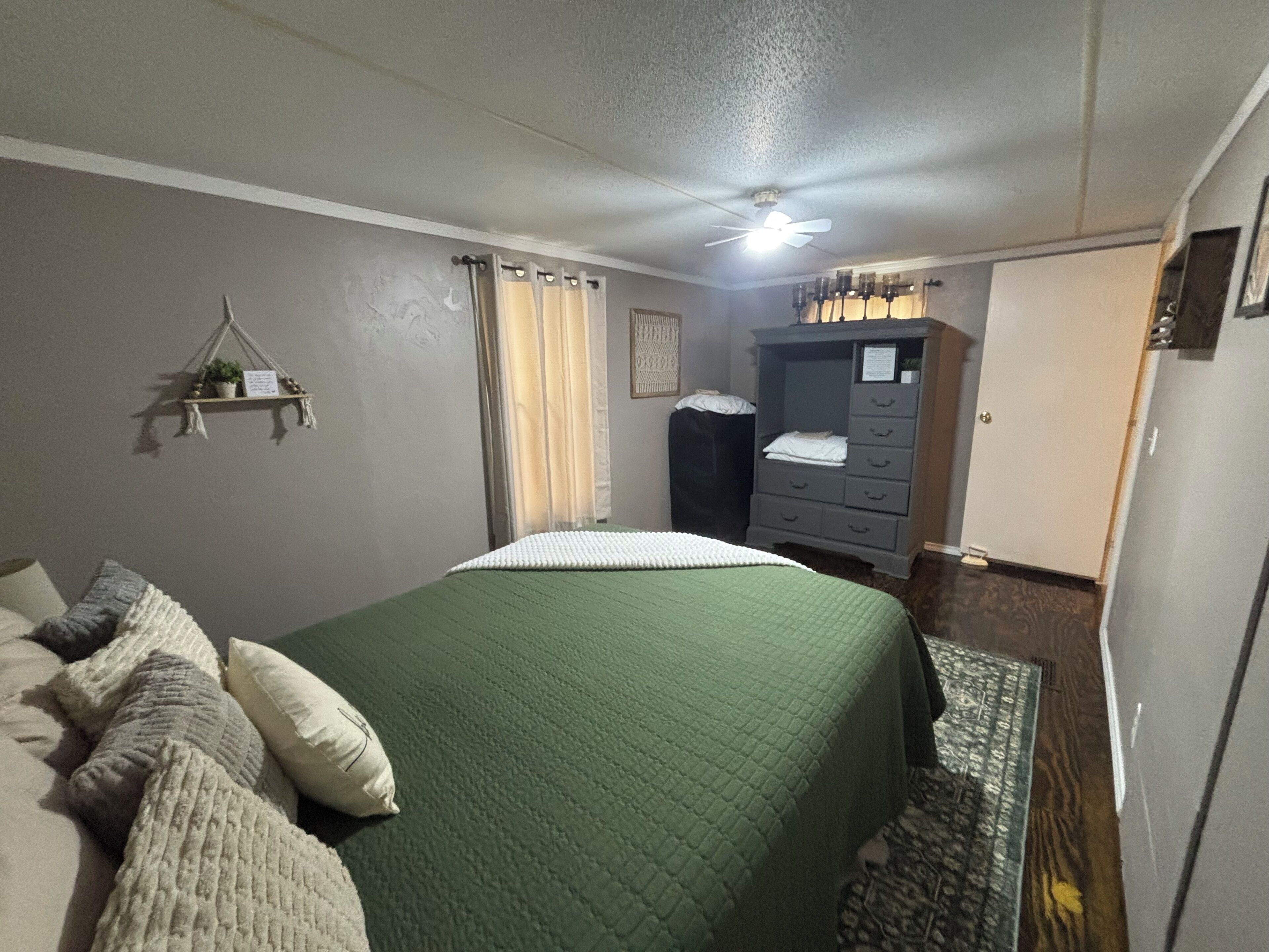 A bedroom with a bed, a dresser, a ceiling fan, and a small plant on a shelf.