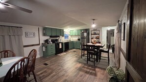Une cuisine avec des meubles de rangement verts, une table à manger avec des chaises et un ventilateur de plafond.