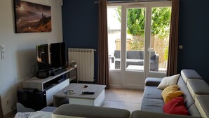 A living room with a television, sofa, and a view of the outdoors through a glass door. - Villa in Provence well located, 90M2 with swimming pool (Auriol)