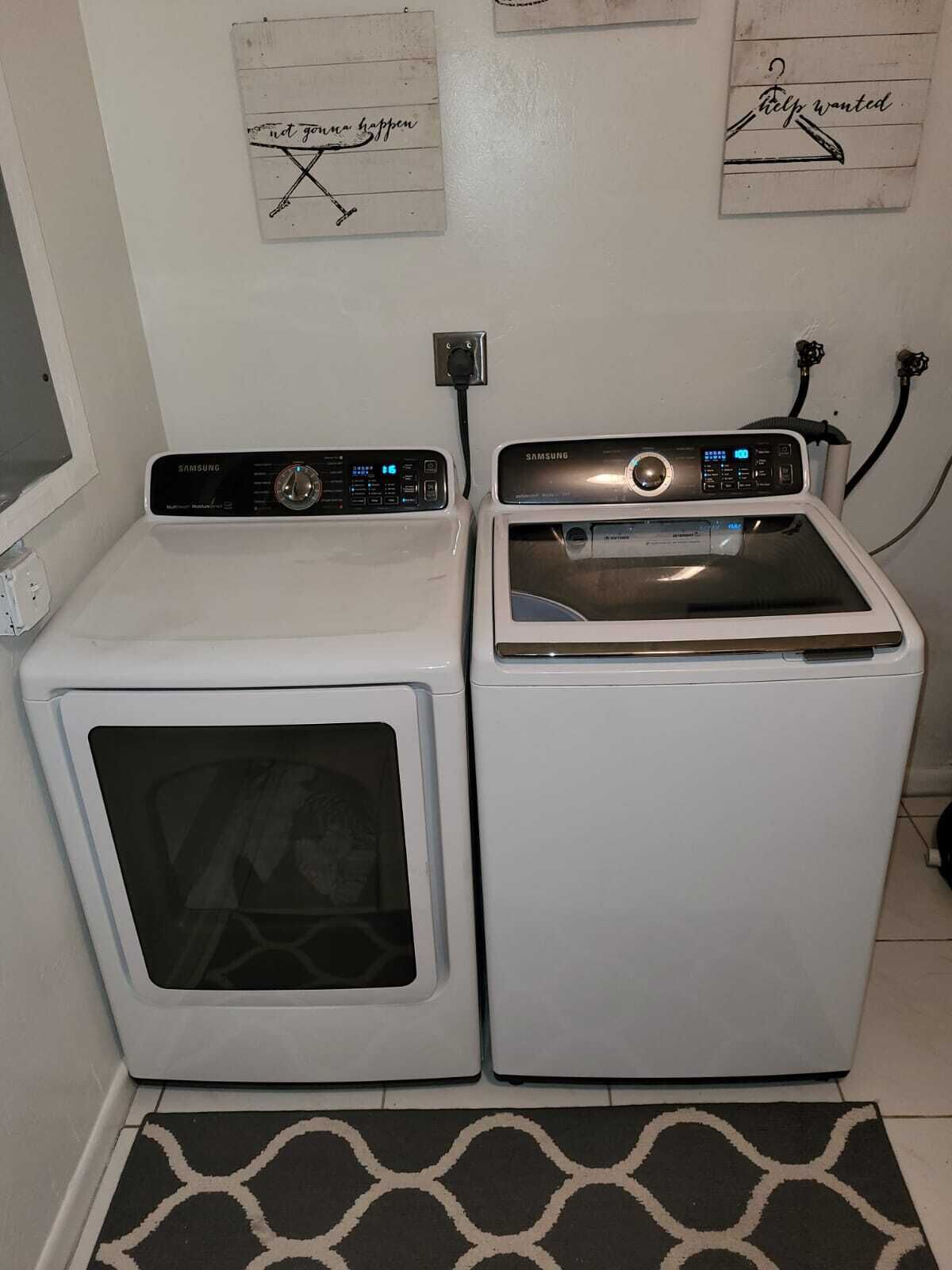 A laundry area with two white washing machines and a dryer, a power outlet, and a wall-mounted electrical outlet.