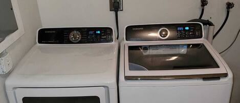 A laundry area with two white washing machines and a dryer, a power outlet, and a wall-mounted electrical outlet.
