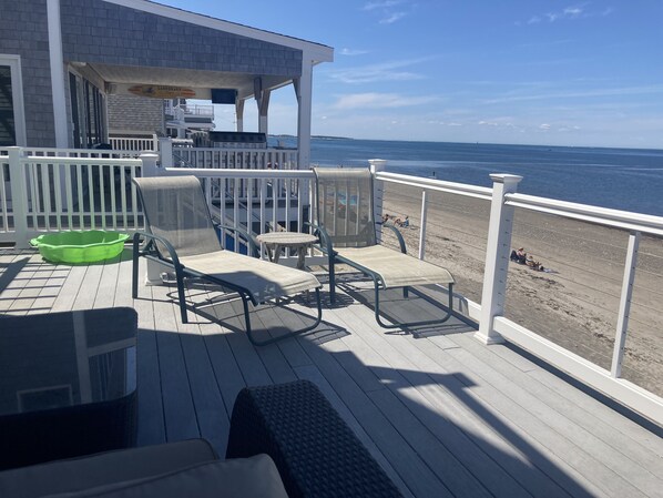 Eine Terrasse mit Sitzgelegenheit, ein grüner Mülleimer und Blick auf den Strand.