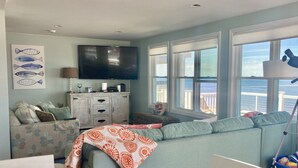 A living room with a large TV, a sofa, a coffee table, and a view of the ocean through large windows. - Scituate oceanfront gem; 5BR  w/ wrap around deck. Perfect for family & friends (Scituate)