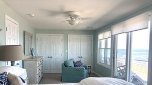 A bedroom with a bed, a chair, a dresser, a ceiling fan, and a view of the ocean through large windows. - Scituate oceanfront gem; 5BR  w/ wrap around deck. Perfect for family & friends (Scituate)