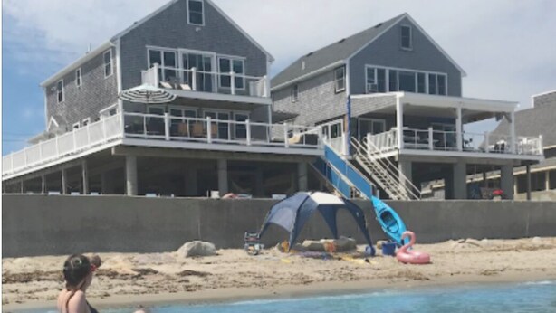 A beachfront property with a large house, a sandy beach, and inflatable rafts in the water. - Scituate oceanfront gem; 5BR  w/ wrap around deck. Perfect for family & friends (Scituate)