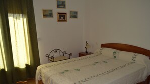 Ein Schlafzimmer mit Bett, Nachttisch, Lampe und einem Fenster mit Vorhängen.