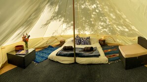A tent with a bed, pillows, a small table with a book, a vase with flowers, and a woven basket. - Glamping in the Redwoods, with hot tub! The Knoll (Garberville)