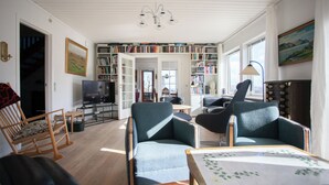 A spacious living room with a wooden floor, a television, a bookshelf, and two armchairs. - Lovely Apartments - 20 min walk from city centre (Tórshavn)