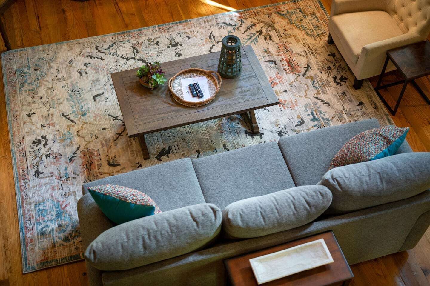 Een gezellige woonkamer met een grijze bank, een houten salontafel en een kamerkleed met een patroon.