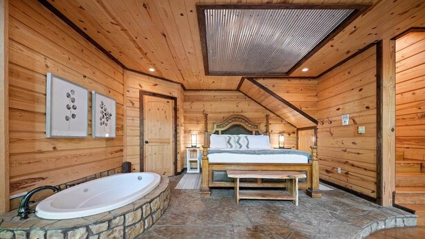 Eine Holzhütte mit einem Badezimmer mit Steinböden, einem Bett mit Kopfteil und gerahmten Kunstwerken an den Wänden.