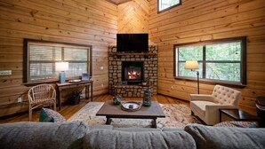 Ein gemütliches Blockhaus-Interieur mit Holzwänden, einem Kamin aus Stein, einem Fernseher und einer bequemen Sitzecke.