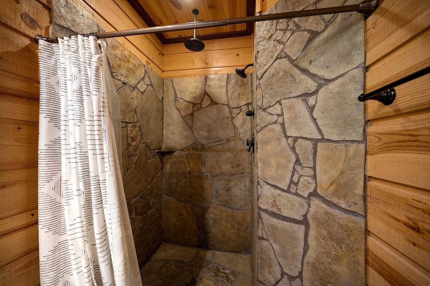 A stone-walled shower with a wooden ceiling and a metal showerhead.