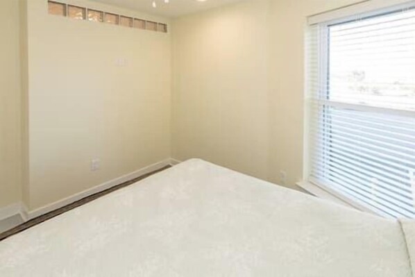 A bedroom with a large bed, a window with blinds, and a plain wall. - Efficiently near beach 302B (Virginia Beach)