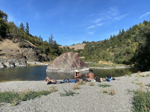 A group of people relaxing by a river with a large rock formation nearby. - Glamping in the Redwoods, with a hot tub! The Orchard (Garberville)