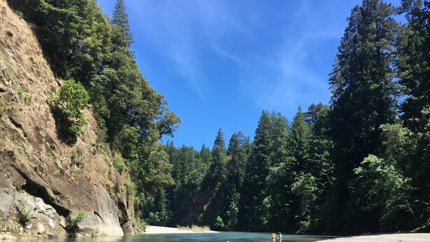 Une rivière bordée d’une forêt dense et de falaises rocheuses.