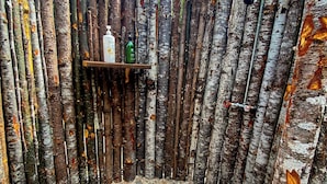 Un espace de douche extérieur rustique, agrémenté de bûches de bouleau, d’une étagère pour les articles de toilette et d’un sol en galets.