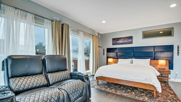 Camera d'albergo moderna con un letto grande, una zona salotto con poltrone in pelle e vista sull'esterno attraverso ampie finestre.