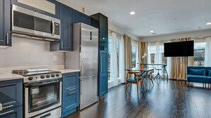 Una cucina moderna con elettrodomestici in acciaio inossidabile, un'area pranzo con tavolo e sedie, e un televisore a schermo piatto montato a parete.