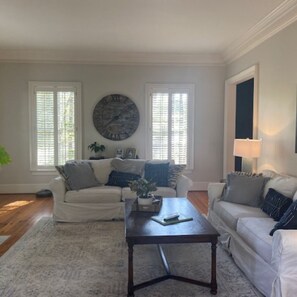 A living room with two white sofas, a dark wooden coffee table, and a large round clock on the wall. - Spacious 5 bedroom, 7 bath Masters rental located 6 miles from course (Evans)