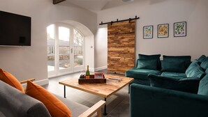 Una sala de estar moderna con un sofá verde, una mesa de centro de madera con una botella y copas, y un televisor montado en la pared.