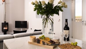 Una sala de estar moderna con una mesa de mármol, un jarrón de rosas blancas, una botella de vino y una chimenea.