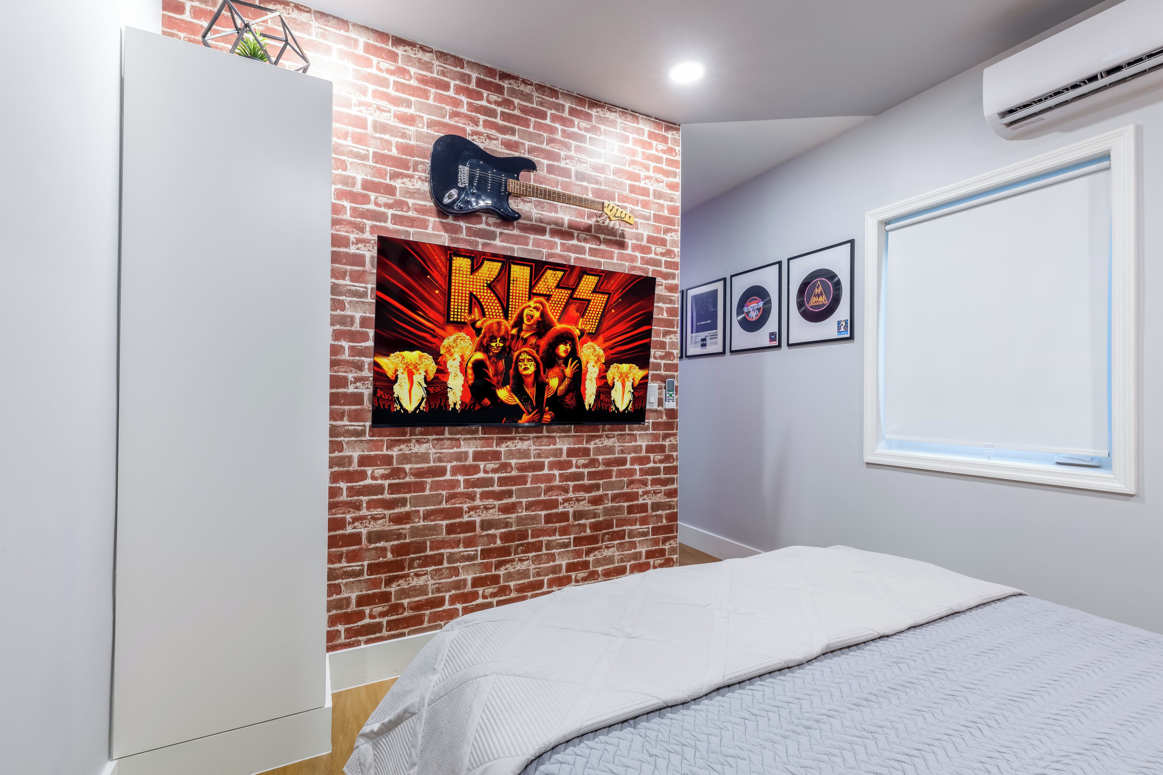A bedroom with a brick wall, a guitar, and framed pictures.