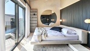 Un dormitorio moderno con una cama grande, un espejo circular y vistas al balcón.