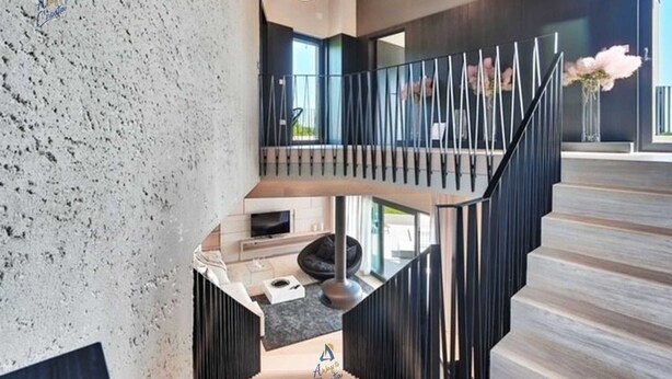 Un interior moderno con una escalera curva, una zona de estar y un ventanal grande.