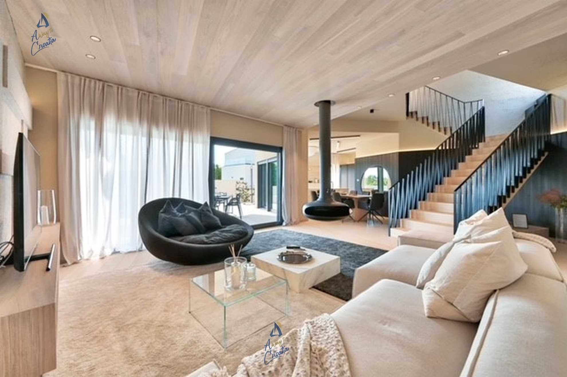 Un salon moderne avec un fauteuil en forme de poire noir, une table basse en verre et un canapé beige. Un escalier mène à un niveau supérieur.