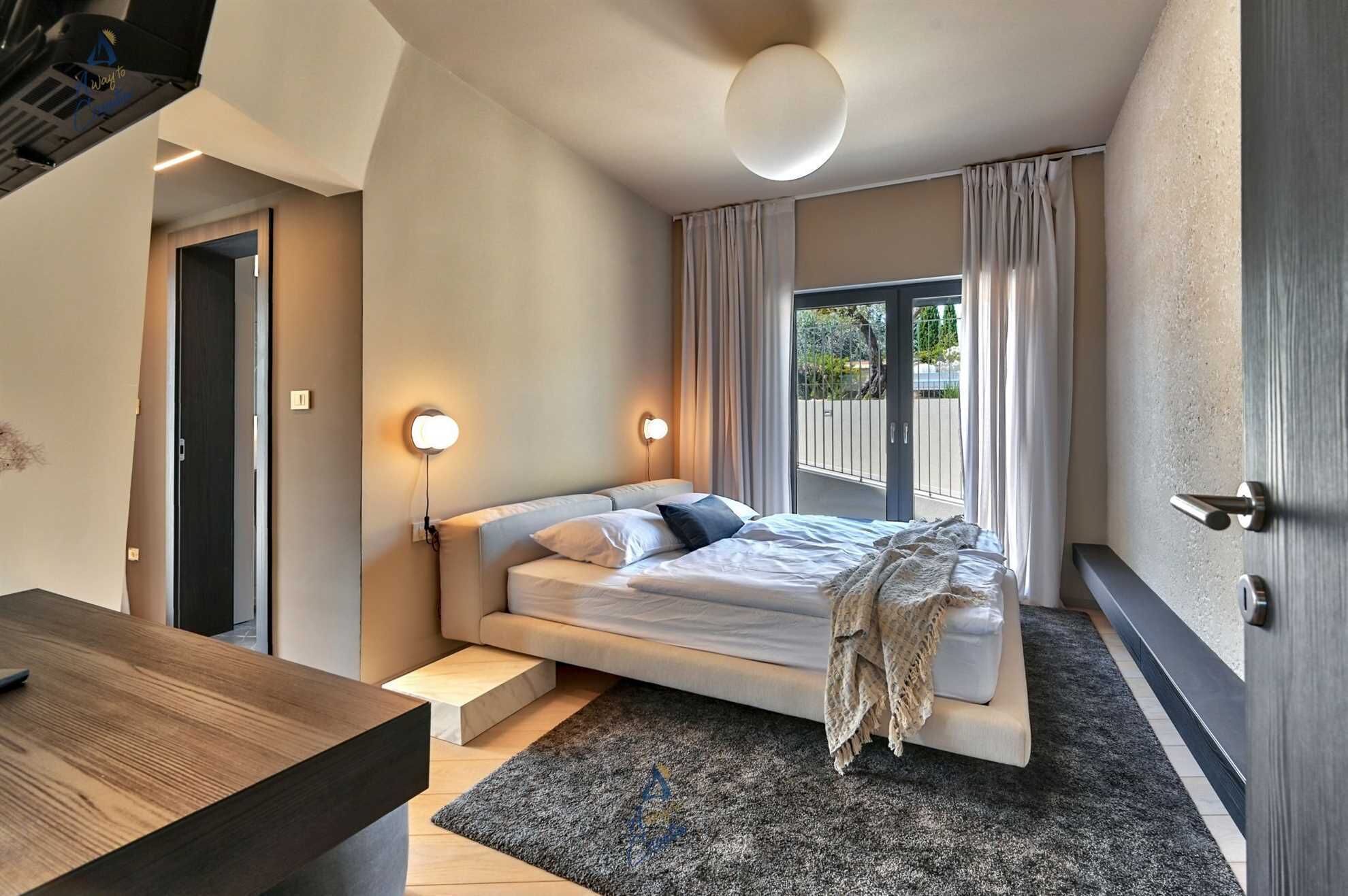 A modern bedroom with a bed, bedside tables, a desk, and a view of the outdoors.