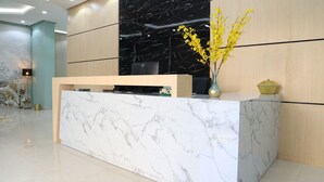 A reception desk with a marble top, a black wall with a marble pattern, and a vase with yellow flowers. - BHomed (Salmiya)