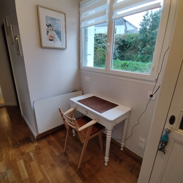 A small kitchen with a wooden chair, a white table, and a window with a view of greenery outside. - Charming little house 5 minutes' walk from the beach (Locquirec)