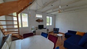 A spacious living area with a dining table, blue and red chairs, a blue sofa, and a staircase. - Charming little house 5 minutes' walk from the beach (Locquirec)
