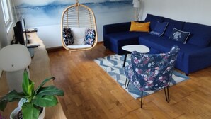 A living room with a hanging chair, a blue sofa, a small round table, and a potted plant. - Charming little house 5 minutes' walk from the beach (Locquirec)
