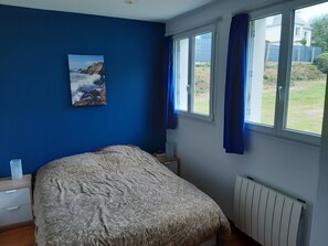 A bedroom with a bed, a nightstand, a window with curtains, and a radiator. - Charming little house 5 minutes' walk from the beach (Locquirec)