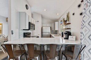 Una cocina moderna con armarios blancos, una isla grande con taburetes y un refrigerador.