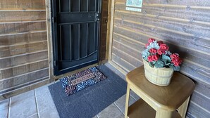 A wooden door with a black panel, a welcome mat, and a small wooden table with a basket of flowers. - Gorgeous 2BR/2BA with Stunning Views and Great Location (Show Low)